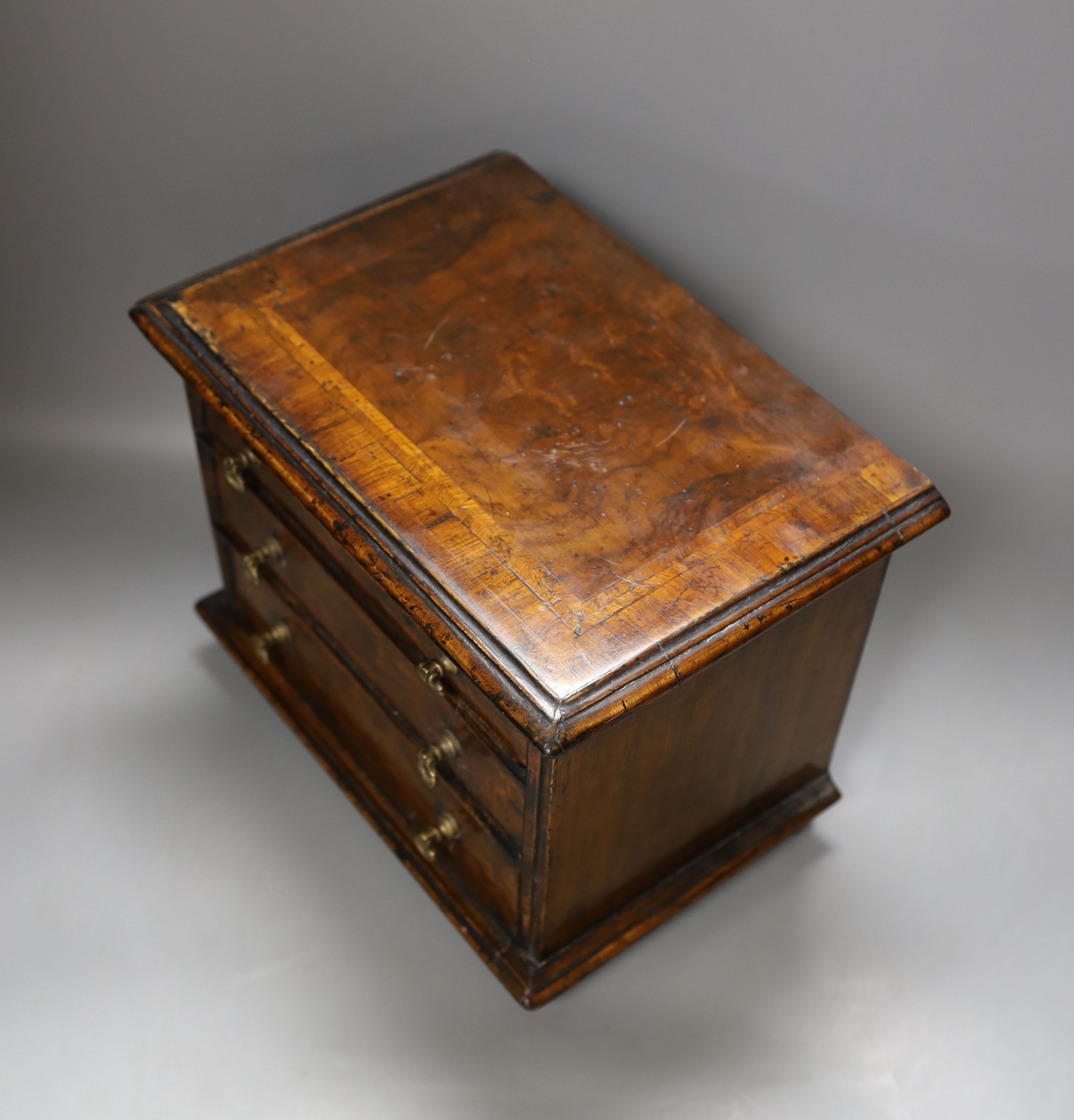 A cross banded walnut miniature chest of three drawers, 26cm wide